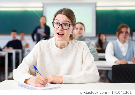 Group of school teenagers with pens and notebooks studying in classroom Group of school teenagers with pens and notebooks studying in classroom 141041301