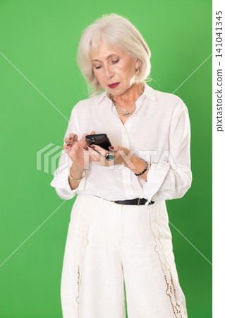 Mature woman in white suit scrolls phone screen, on green screen background Mature woman in white suit scrolls phone screen, on green screen background 141041345