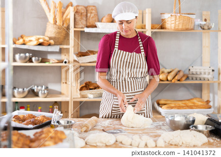 Woman works in bakery as baker, kneads dough, works with flour. 141041372