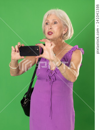 Elderly woman taking photo or scanning QR code with smartphone on green screen Elderly woman taking photo or scanning QR code with smartphone on green screen 141041386