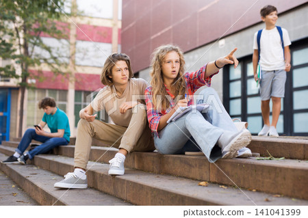 Girl points her hand at someone on the street to guy during break in college Girl points her hand at someone on the street to guy during break in college 141041399