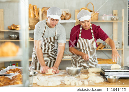 Two bakers work together to prepare dough and weigh it on scales to make croissants Two bakers work together to prepare dough and weigh it on scales to make croissants 141041455