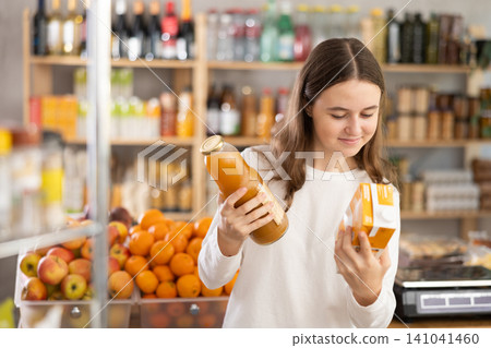 Teen girl hold packages bottles and choose consider juice in store Teen girl hold packages bottles and choose consider juice in store 141041460