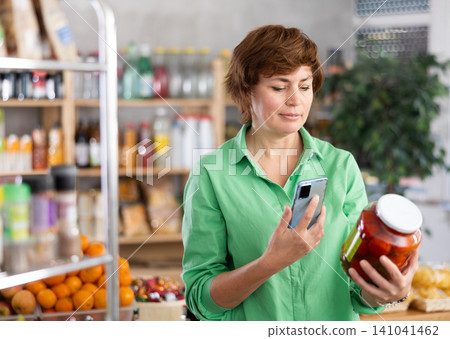 Woman customer holds jar of canned tomato in hand, scans QR code on product label 141041462