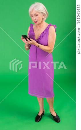 Mature woman in pink dress scrolling through smartphone screen against a green screen background. Chroma key compositing Mature woman in pink dress scrolling through smartphone screen against a green screen background. Chroma key compositing 141041483
