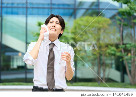 A businessman wiping sweat from his brow in the hot outdoors. A businessman wiping sweat from his brow in the hot outdoors. 141041499