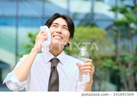 一位商人正在炎熱的戶外擦拭額頭的汗水。 141041504