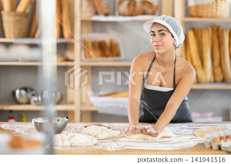 Young woman baker kneads the dough in bakery Young woman baker kneads the dough in bakery 141041516