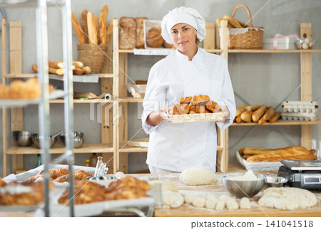 In working room of bakery, there is woman with croissants in wicker basket in hands In working room of bakery, there is woman with croissants in wicker basket in hands 141041518
