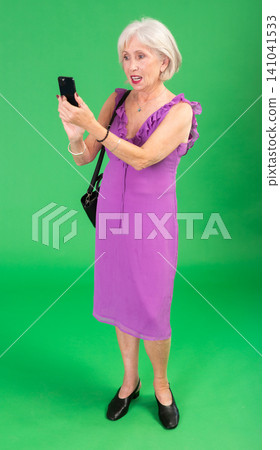 Elderly woman in pink dress scans QR code or takes photo with a smartphone. Green background. Chroma key compositing Elderly woman in pink dress scans QR code or takes photo with a smartphone. Green background. Chroma key compositing 141041533