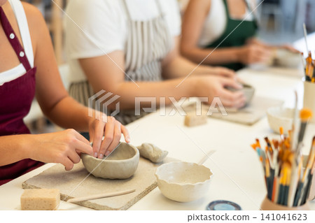 Girl hands forms bowl of clay during master class, close up Girl hands forms bowl of clay during master class, close up 141041623