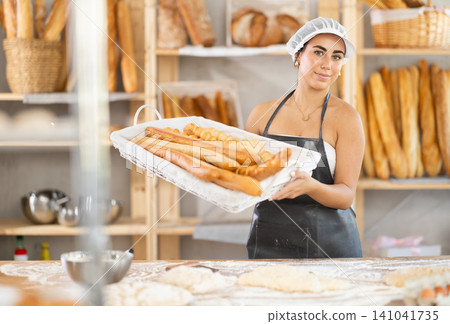 Young female baker with basket of baguettes 141041735