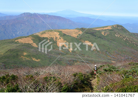Hikers heading towards Mount Matatake via the Tenma Ridge from Mount Kurikoma in autumn, with Mount Chokai visible in the distance beyond the mountains. Hikers heading towards Mount Matatake via the Tenma Ridge from Mount Kurikoma in autumn, with Mount Chokai visible in the distance beyond the mountains. 141041767