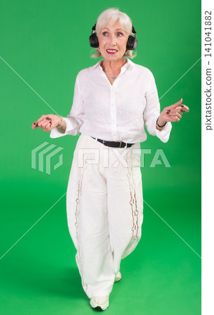 Elderly woman listening to music and dancing in front of green screen Elderly woman listening to music and dancing in front of green screen 141041882