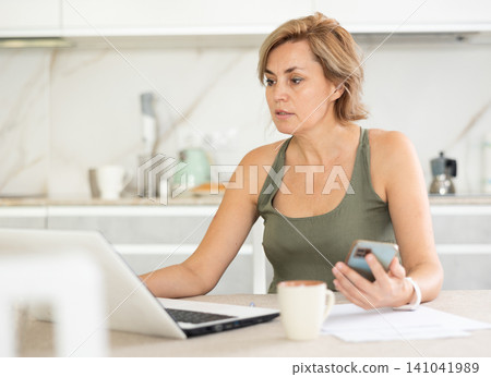 Woman chatting on internet using laptop in domestic kitchen Woman chatting on internet using laptop in domestic kitchen 141041989