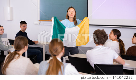 High school teacher tells students about Ireland and holds a Ireland flag in hands. High school teacher tells students about Ireland and holds a Ireland flag in hands. 141042252