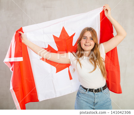 Joyful female fan of the favorite team of Canada with the national flag in hands Joyful female fan of the favorite team of Canada with the national flag in hands 141042306