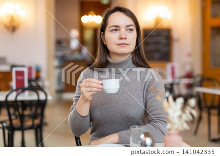 Brunette sitting in cozy cafe with cup of coffee Brunette sitting in cozy cafe with cup of coffee 141042335