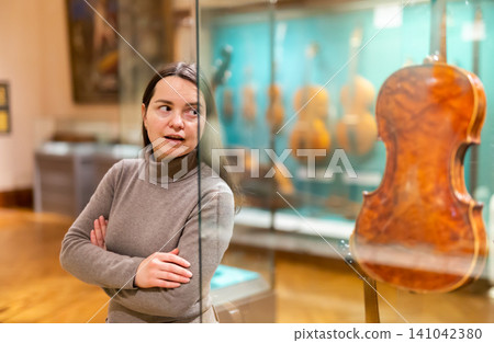Surprised woman viewing antique violin in museum of musical instruments Surprised woman viewing antique violin in museum of musical instruments 141042380
