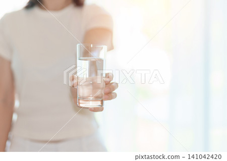 Healthy woman hold glass of clean mineral water glass on sofa at home, female drink pure water for hydration and wellness, fresh skin care, daily routine water intake, Refreshment and lifestyle Healthy woman hold glass of clean mineral water glass on sofa at home, female drink pure water for hydration and wellness, fresh skin care, daily routine water intake, Refreshment and lifestyle 141042420