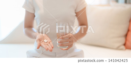 woman hand holding medicine painkiller pill and water glass on the sofa at home, taking for headaches, stomach ache, Diarrhea Pain from food poisoning, Endometriosis, Hysterectomy and Menstrual woman hand holding medicine painkiller pill and water glass on the sofa at home, taking for headaches, stomach ache, Diarrhea Pain from food poisoning, Endometriosis, Hysterectomy and Menstrual 141042425