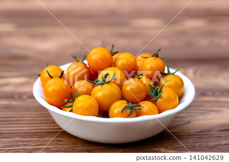 Orange cherry tomatoes in a bowl on the wooden table in the garden. Orange cherry tomatoes in a bowl on the wooden table in the garden. 141042629