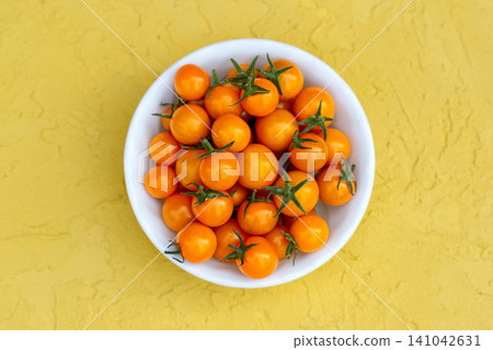 Vivid orange cherry tomatoes in a bowl on the yellow table. 141042631