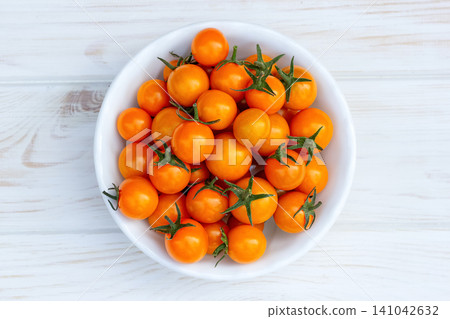 Orange cherry tomatoes in a bowl on the white wooden table. 141042632