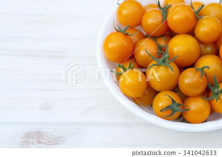 Orange cherry tomatoes in a bowl on the white wooden table. Orange cherry tomatoes in a bowl on the white wooden table. 141042633