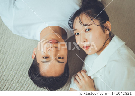 A bird's-eye view portrait of a couple on a rug, with the woman gazing at the camera with a calm expression and the boyfriend lying on his back. 141042821