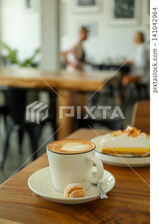 A cup of coffee sits on a table with a dessert nearby 141042964