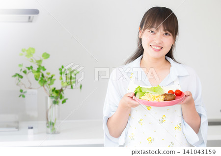 A woman preparing dinner and home-cooked meals for her mother and family; an image of a housewife or domestic helper, looking directly at the camera and smiling. 141043159