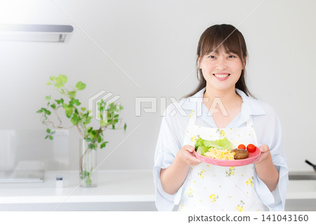 一位女性正在為她的母親和家人準備晚餐和家常菜;一位家庭主婦或家政工人的形象,她直視鏡頭,面帶微笑。 一位女性正在為她的母親和家人準備晚餐和家常菜;一位家庭主婦或家政工人的形象,她直視鏡頭,面帶微笑。 141043160