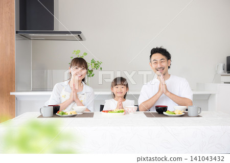 一家三口,包括一位家長和一個孩子,在餐桌旁坐下,說著「いただきます」(謝謝款待),開始用餐。這張照片展現了食物教育和家庭團聚的重要性,鏡頭直視鏡頭。 一家三口,包括一位家長和一個孩子,在餐桌旁坐下,說著「いただきます」(謝謝款待),開始用餐。這張照片展現了食物教育和家庭團聚的重要性,鏡頭直視鏡頭。 141043432