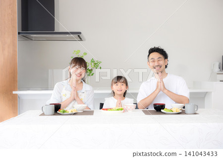 一家三口,包括一位家長和一個孩子,在餐桌旁坐下,說著「いただきます」(謝謝款待),開始用餐。這張照片展現了食物教育和家庭團聚的重要性,鏡頭直視鏡頭。 一家三口,包括一位家長和一個孩子,在餐桌旁坐下,說著「いただきます」(謝謝款待),開始用餐。這張照片展現了食物教育和家庭團聚的重要性,鏡頭直視鏡頭。 141043433