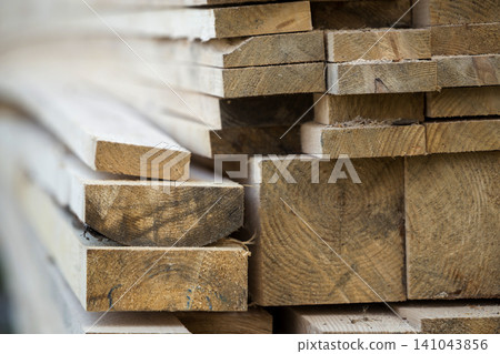 Stack of natural brown uneven rough wooden boards different size, cross-sectional view. Industrial timber for carpentry, building, repairing and furniture, lumber material for construction. Stack of natural brown uneven rough wooden boards different size, cross-sectional view. Industrial timber for carpentry, building, repairing and furniture, lumber material for construction. 141043856