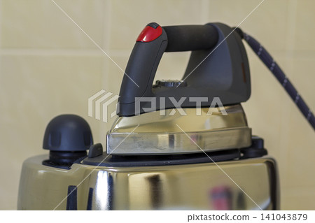 Close-up of new modern stainless steel iron with teflon sole and with steam generator isolated on iron plate on light copy space background. Close-up of new modern stainless steel iron with teflon sole and with steam generator isolated on iron plate on light copy space background. 141043879
