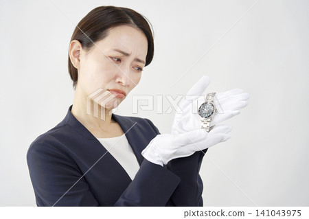 A female appraiser with a troubled expression, holding a wristwatch, against a white background. A female appraiser with a troubled expression, holding a wristwatch, against a white background. 141043975