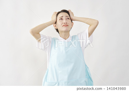 A female caregiver holding her head against a white background. A female caregiver holding her head against a white background. 141043980
