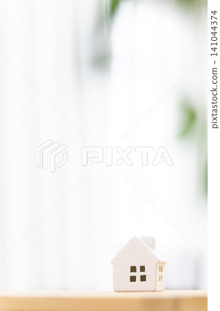一間光線明亮的房間裡,桌上擺放著一棟微型房屋(我的家/住宅),並留有文字空間。 一間光線明亮的房間裡,桌上擺放著一棟微型房屋(我的家/住宅),並留有文字空間。 141044374