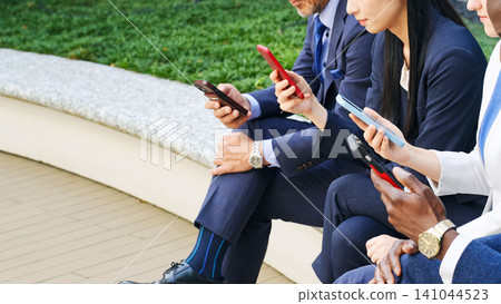 A group of multinational business people looking at their smartphones on an outdoor bench A group of multinational business people looking at their smartphones on an outdoor bench 141044523