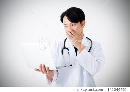 A middle-aged male doctor in a white coat looks surprised when he sees a laptop. A middle-aged male doctor in a white coat looks surprised when he sees a laptop. 141044761