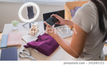 Asian woman online merchant taking product photos of purple clothing using smartphone and ring light at workspace Asian woman online merchant taking product photos of purple clothing using smartphone and ring light at workspace 141045151