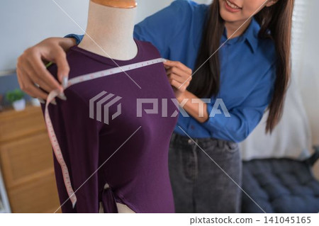 Young Asian female online merchant measuring purple dress on mannequin in home studio workspace Young Asian female online merchant measuring purple dress on mannequin in home studio workspace 141045165