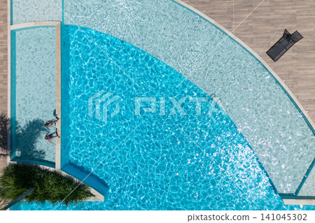 Two kids relax at the edge of clear blue pool during sunny summer vacation. This aerial view captures family, friends, fun, and recreation at resort, relaxation and joyful outdoor moments. Two kids relax at the edge of clear blue pool during sunny summer vacation. This aerial view captures family, friends, fun, and recreation at resort, relaxation and joyful outdoor moments. 141045302