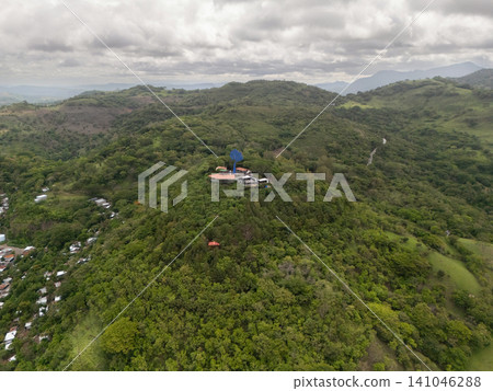 View of a green hill with buildings and trees under a cloudy sky 141046288