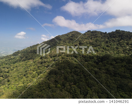 Mountains covered in green trees with blue sky and clouds above Mountains covered in green trees with blue sky and clouds above 141046291