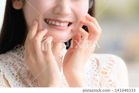 一位年輕的日本女子麵帶微笑,撫摸著自己的臉頰。 一位年輕的日本女子麵帶微笑,撫摸著自己的臉頰。 141046335