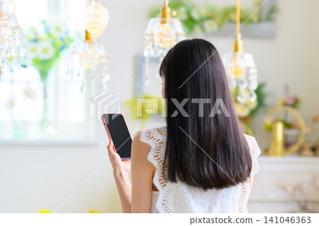 A woman's back view as she holds a smartphone indoors. A woman's back view as she holds a smartphone indoors. 141046363
