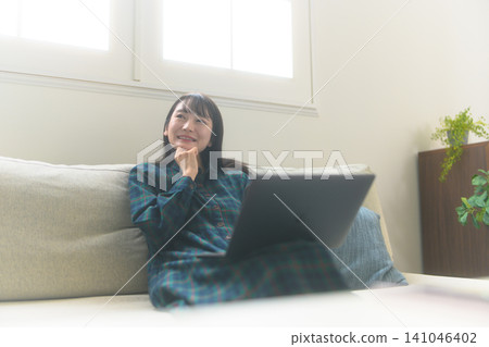 一位女士坐在沙發上,盯著她的筆記型電腦。 一位女士坐在沙發上,盯著她的筆記型電腦。 141046402